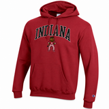 A red pullover hoodie featuring the word 'INDIANA' in arched black letters with a white outline on the chest, and an Indiana Bear mascot graphic below it. A small Champion logo is visible on the left sleeve cuff.